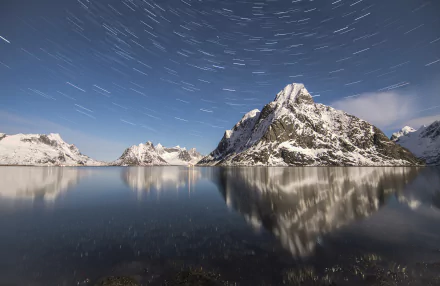 4K Ultra HD wallpaper of a snow-covered mountain reflected in a lake under a star-filled winter sky with visible star trails, showcasing serene natural beauty.