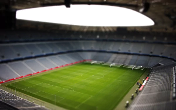 A tilt-shift aerial view of a Munich soccer stadium, captured in vibrant 4K Ultra HD, highlighting the green pitch and surrounding empty stands.