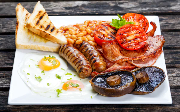 A 4K Ultra HD desktop wallpaper of a full English breakfast featuring beans, toast, bacon, sausage, grilled mushroom, fried eggs, and roasted tomatoes on a white plate.