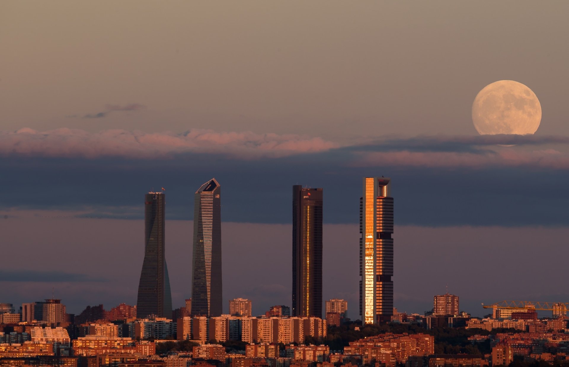 Skyline of Madrid, Spain featuring prominent skyscrapers under a large moon at dusk, captured in an HD cityscape wallpaper.