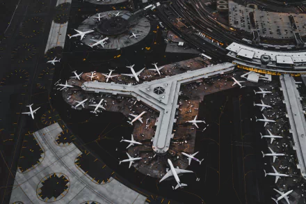 A high-definition aerial view of a busy airport with multiple aircraft parked around terminals. This image captures the intricate layout and bustling activity of a major transportation hub.