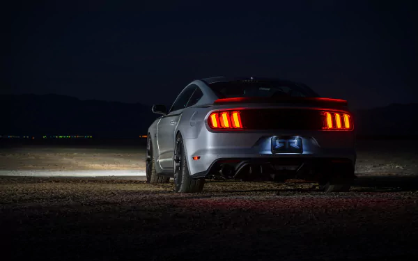 Rear view of a silver Ford Mustang RTR muscle car parked at night, highlighting its illuminated taillights against a dark backdrop.