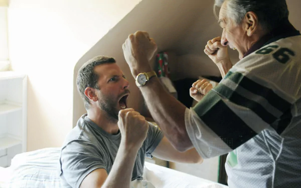 HD PC desktop wallpaper: two men playfully sparring on a bed in a sunlit room — a cinematic scene inspired by the movie Silver Linings Playbook.