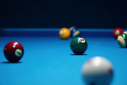 HD desktop wallpaper of a blue pool table in action, featuring various bright, numbered billiard balls positioned around the table, creating a dynamic and engaging scene.