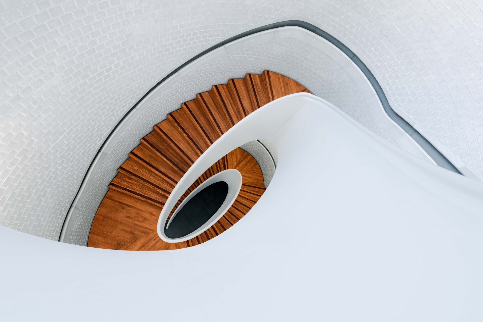 Top-down view of a man-made spiral staircase with warm wooden steps and white curved walls — 5K Ultra HD PC desktop wallpaper/background.