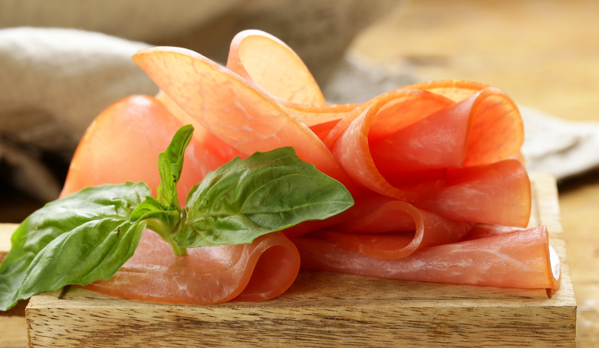 2K Quad HD PC desktop wallpaper of thinly sliced cured meat arranged on a wooden board with fresh basil leaves.