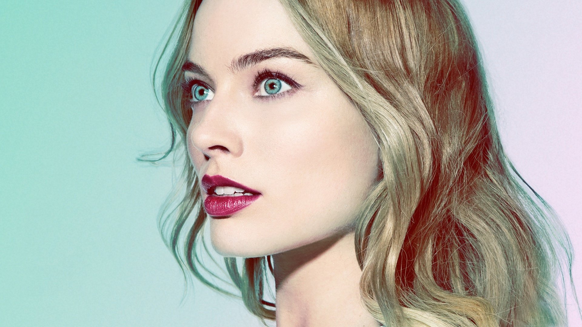 HD desktop wallpaper of Australian actress Margot Robbie with blonde hair, blue eyes, and red lipstick, showcasing a close-up of her face with a soft, colorful background.