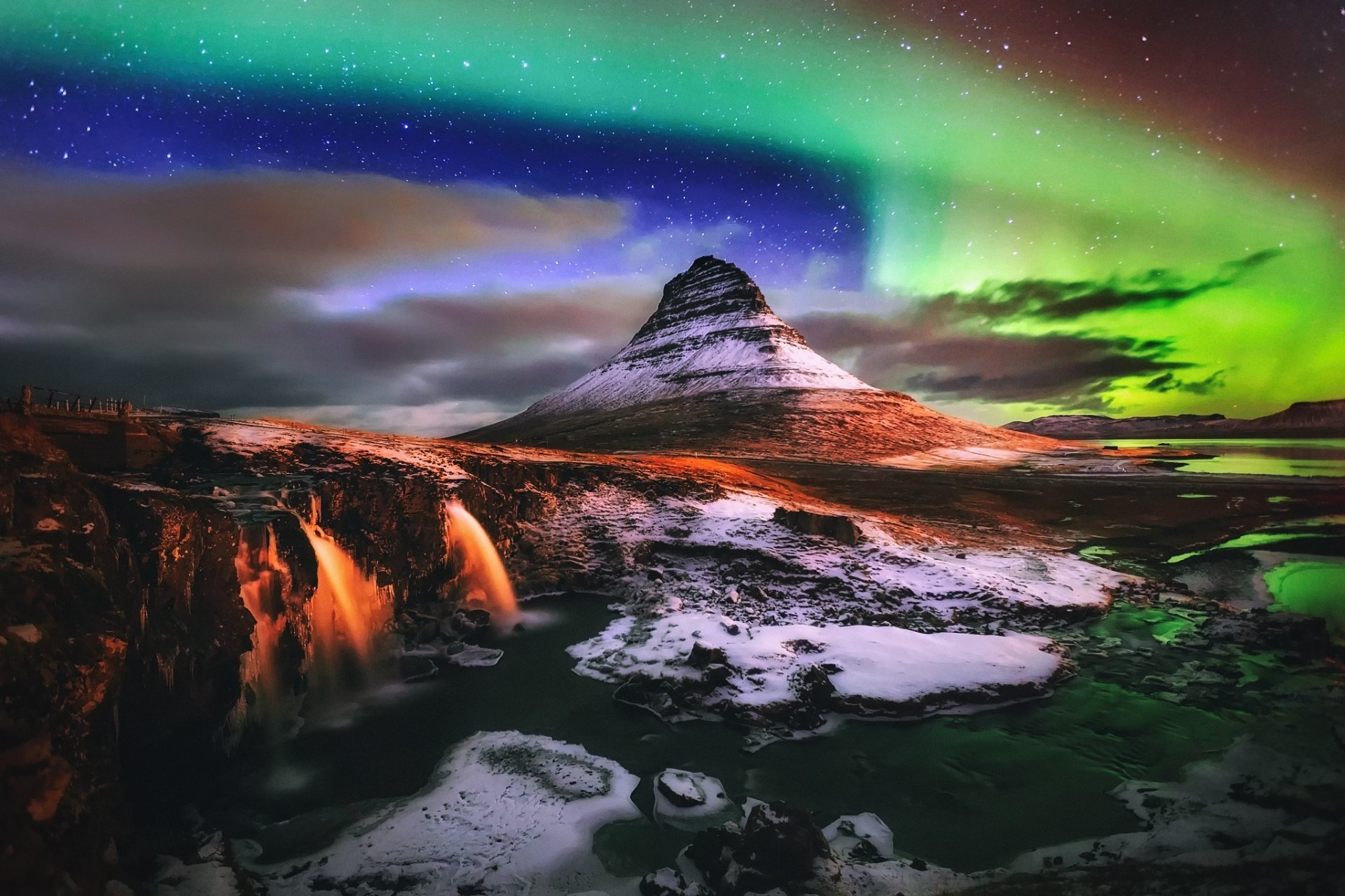 Aurora borealis lights up the night sky above Kirkjufoss waterfall and Kirkjufell mountain in winter, showcasing Iceland's stunning natural beauty.