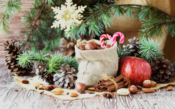 Holiday-themed HD desktop wallpaper featuring pine cones, a red apple, cinnamon sticks, candy canes, and festive greenery arranged on a rustic wooden surface.