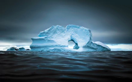 A stunning HD desktop wallpaper of a large iceberg floating in a dark, serene ocean under a moody sky.
