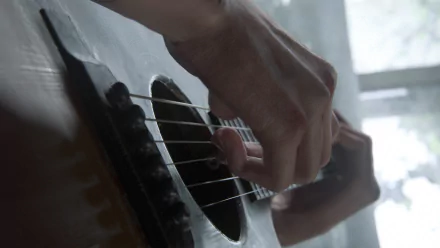 A high-definition desktop wallpaper from The Last of Us Part II, showcasing a close-up of a hand strumming an acoustic guitar.
