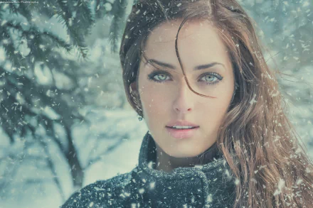 HD desktop wallpaper featuring a brunette woman with green eyes, standing against a snowy backdrop, with snowfall gently landing around her.