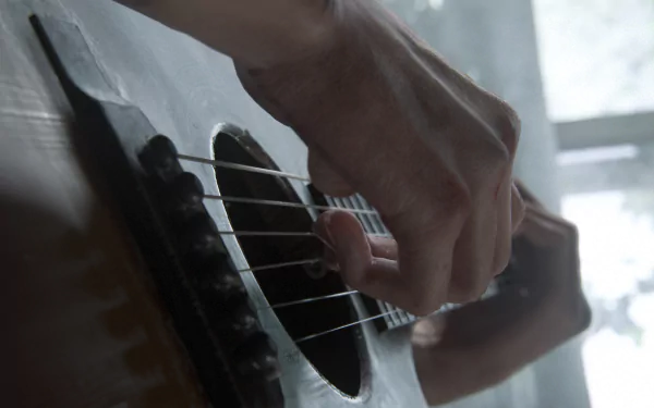 A high-definition desktop wallpaper from The Last of Us Part II, showcasing a close-up of a hand strumming an acoustic guitar.