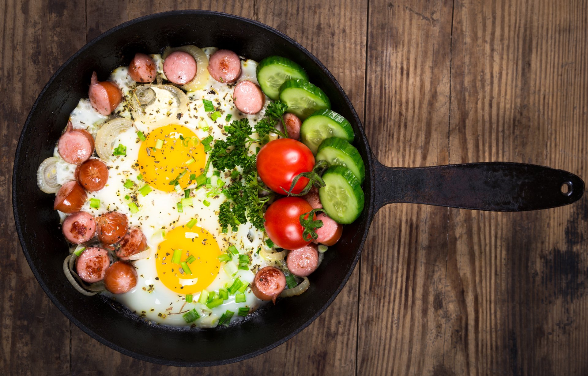 5K Ultra HD PC desktop wallpaper: a skillet with two sunny-side-up eggs, sliced sausages, cucumber rounds and cherry tomatoes on a rustic wooden background.