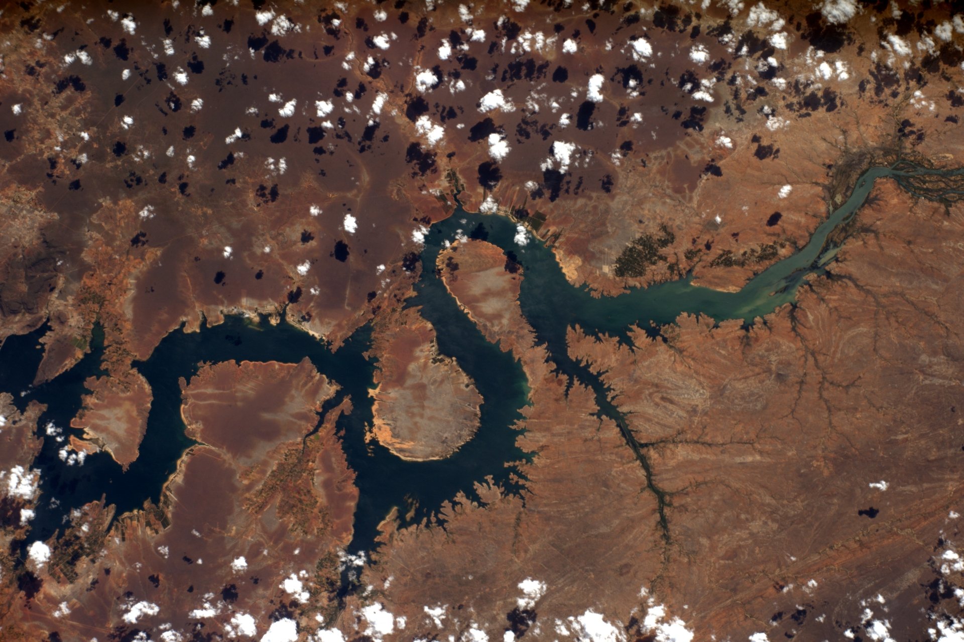 Aerial landscape photography of a winding river carving rust-colored terrain dotted with clouds — 4K Ultra HD PC desktop wallpaper and background.