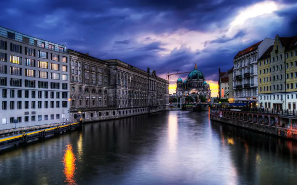 Dusk over the river in Berlin, featuring the illuminated Berlin Cathedral and surrounding man-made buildings reflected on the water in this HD desktop wallpaper.