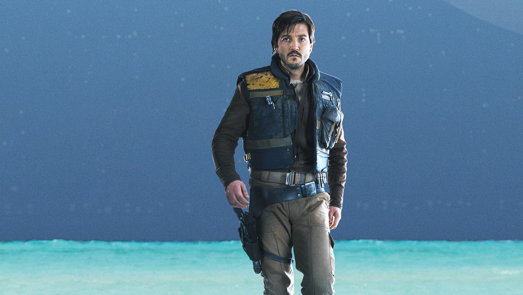 HD PC desktop wallpaper of a rugged rebel operative from the movie Rogue One standing on a turquoise shoreline beneath a starry sky.
