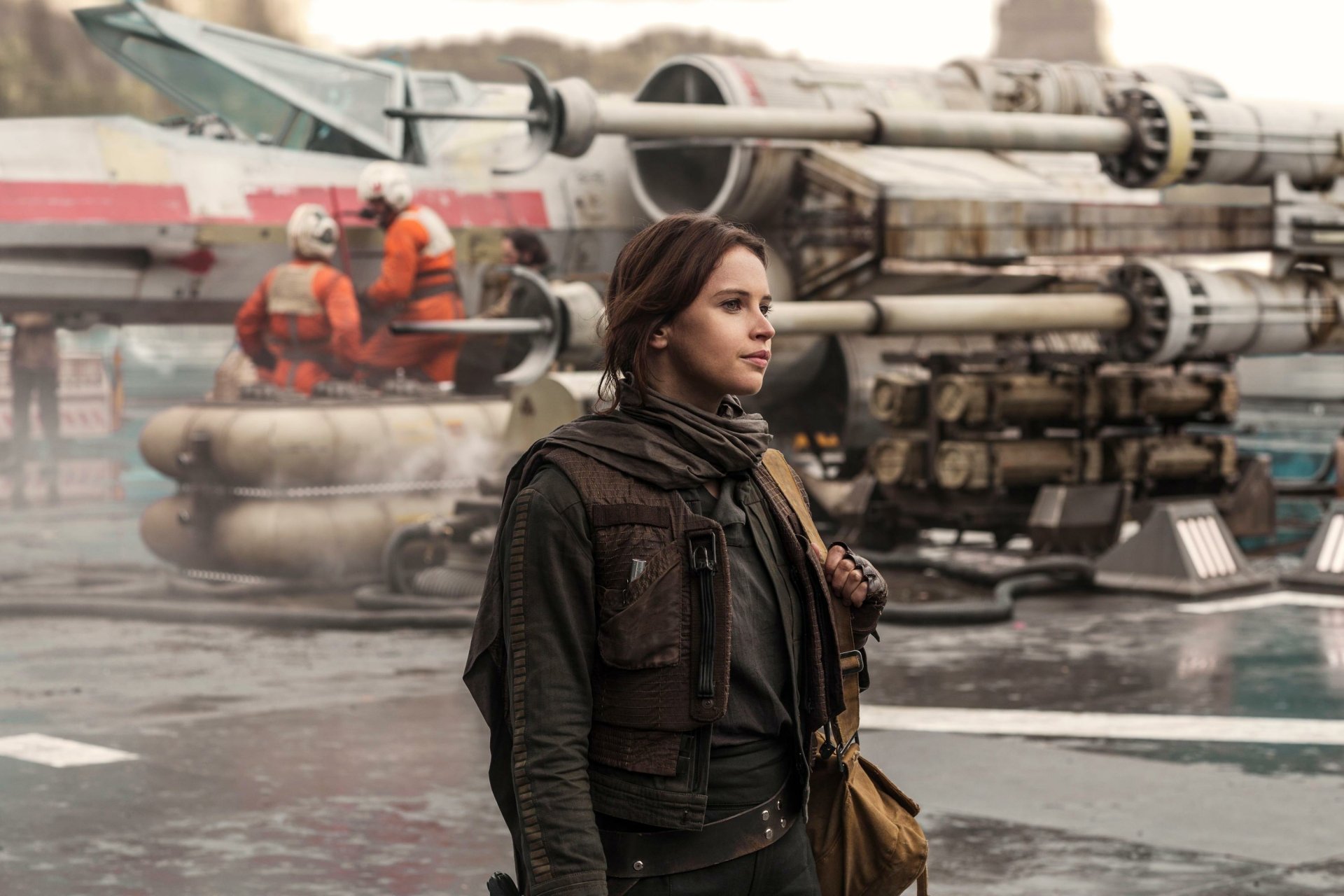 HD wallpaper featuring Jyn Erso (Felicity Jones) from the movie Rogue One: A Star Wars Story, standing in front of a starship with crew members in the background.
