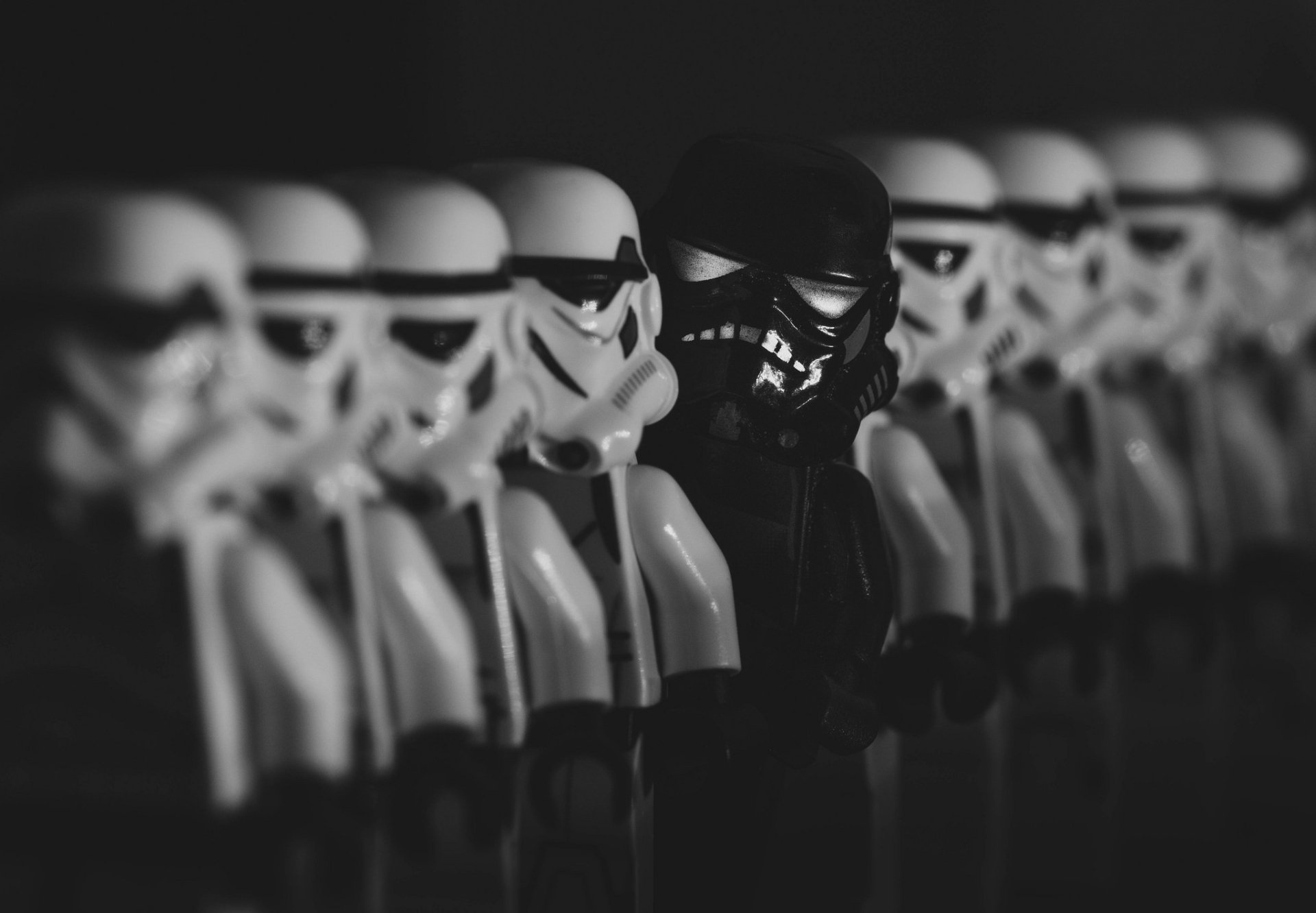 Black-and-white HD PC desktop wallpaper showing Lego Star Wars stormtroopers in a row: white troopers flanking a single black trooper, man-made toy figures in shallow focus.