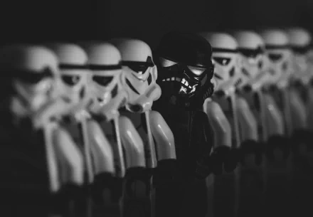 Black-and-white HD PC desktop wallpaper showing Lego Star Wars stormtroopers in a row: white troopers flanking a single black trooper, man-made toy figures in shallow focus.
