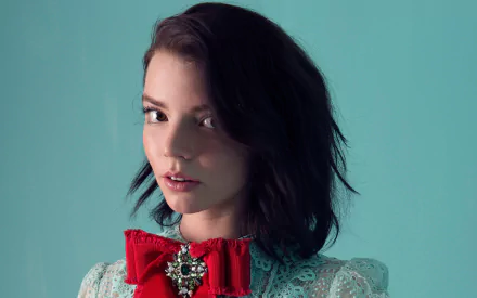 HD desktop wallpaper featuring American actress and model Anya Taylor-Joy with brunette hair, brown eyes, and a red bow accessory against a teal background.
