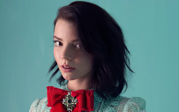 HD desktop wallpaper featuring American actress and model Anya Taylor-Joy with brunette hair, brown eyes, and a red bow accessory against a teal background.