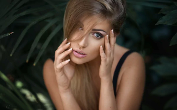 HD desktop wallpaper featuring a close-up of blonde model Lina Roth’s face framed by dark foliage, highlighting her striking blue eyes and natural beauty.