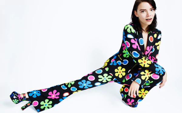Anya Taylor-Joy, American actress with brown eyes and brunette hair, poses confidently in a colorful floral jumpsuit against a white background.