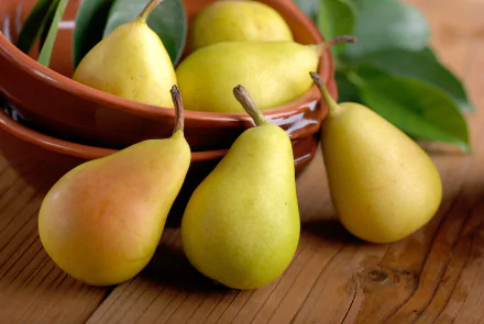 A 4K Ultra HD PC desktop wallpaper featuring fresh yellow pears arranged on and around stacked brown bowls with green leaves and a wooden surface background.