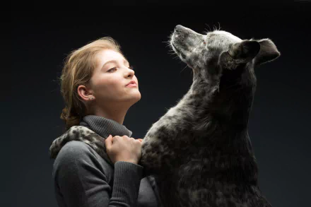 Blonde American actress Willow Shields embraces a large dog with brown eyes against a dark background in this 4K Ultra HD PC desktop wallpaper.