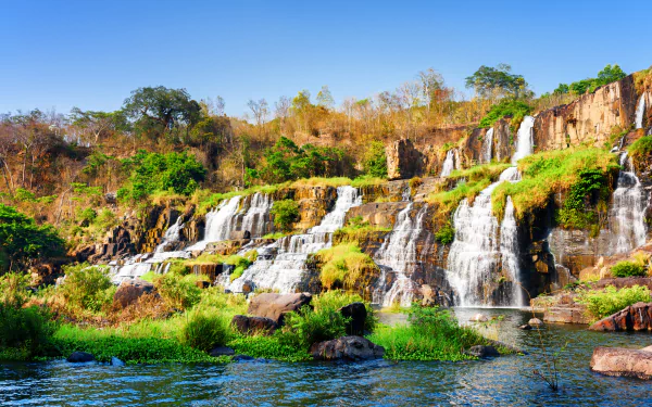 A vibrant 4K Ultra HD wallpaper of Pongour Waterfall in Vietnam showcasing cascading water over rocky cliffs surrounded by lush greenery and clear blue sky.