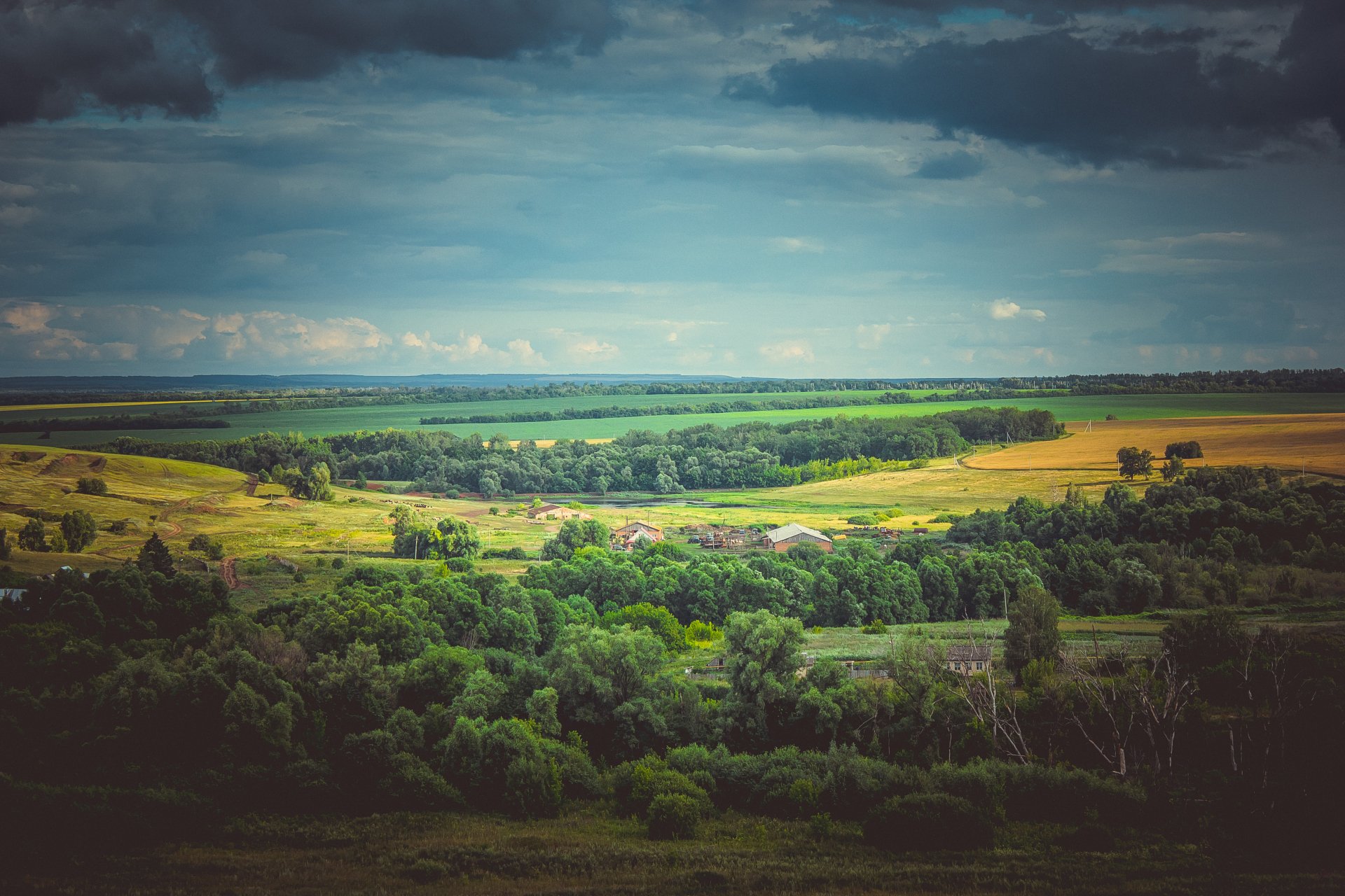 4K Ultra HD landscape of a Russian countryside featuring a green forest, expansive fields, a village, and a cloudy sky stretching along the horizon.