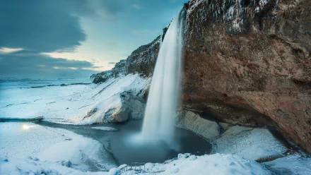 HD desktop wallpaper of Seljalandsfoss waterfall in Iceland. The stunning winter landscape features snow-covered terrain and a majestic waterfall cascading over a rocky cliff.