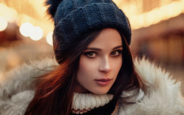 A striking model with red hair and hazel eyes wears a cozy hat, set against a bokeh background. This HD image captures her captivating expression and stylish look.
