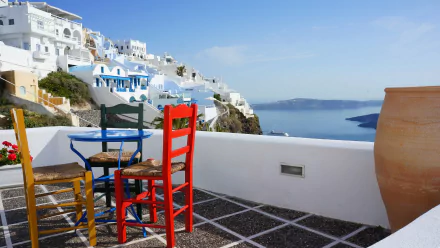 4K Ultra HD wallpaper showing colorful chairs on a white porch overlooking iconic white houses and blue domes of Santorini against a clear sky.