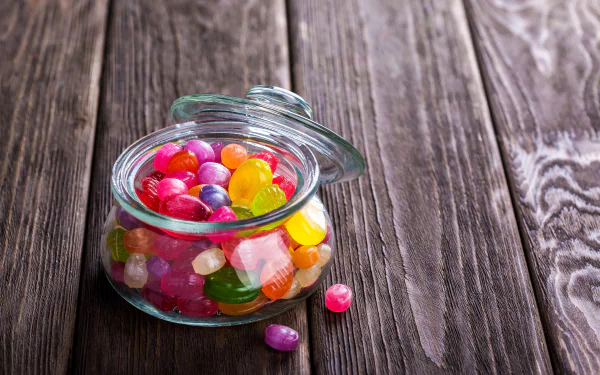A vibrant jar filled with colorful sweets and candies on a rustic wooden surface, captured in sharp 4K Ultra HD quality as a PC desktop wallpaper background.