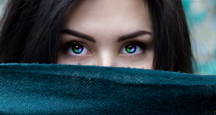Close-up of a woman's face with striking green eyes, partially covered by a teal fabric, framed by dark hair. This HD desktop wallpaper makes a captivating background.