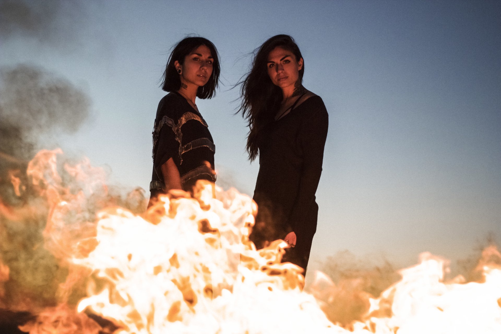 HD PC desktop wallpaper featuring Krewella standing behind a blazing fire under a clear sky, capturing a dramatic and intense music-themed scene.