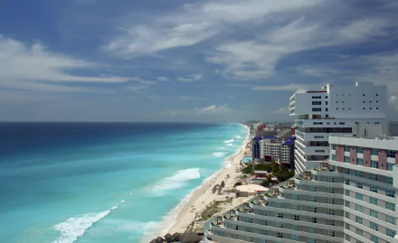 Turquoise ocean waves meet a sandy beach along the horizon, framed by a man-made resort and hotels in Cancún, Mexico.