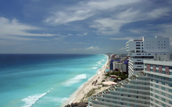 Turquoise ocean waves meet a sandy beach along the horizon, framed by a man-made resort and hotels in Cancún, Mexico.