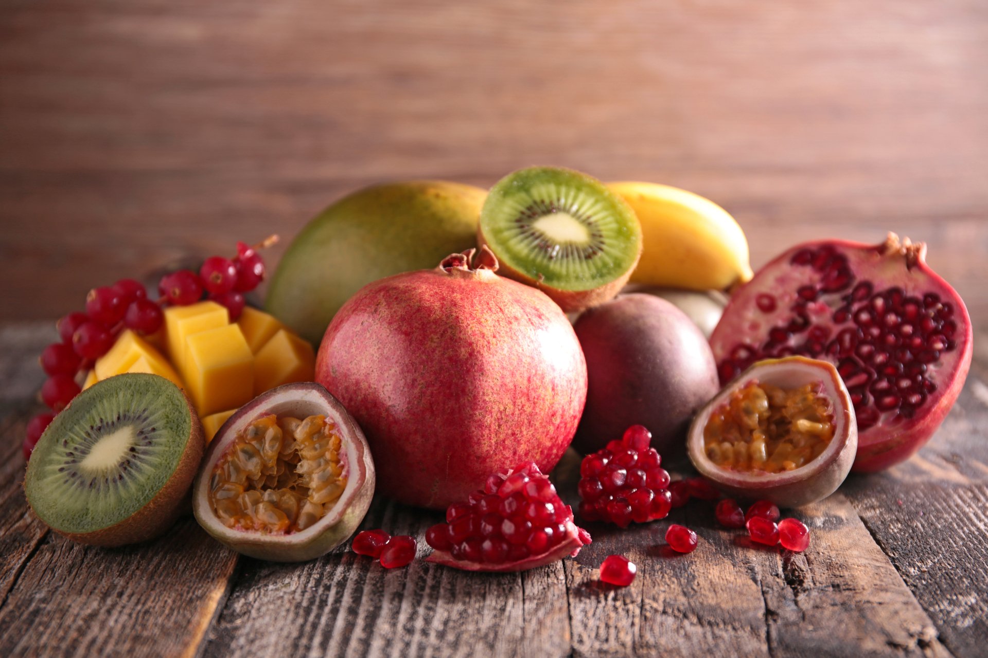 5K Ultra HD PC desktop wallpaper of assorted fruit: whole and cut mango, pomegranate, kiwi, passionfruit and more arranged on rustic wood — vibrant food background.