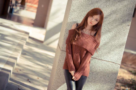 Image of an Asian woman with red hair posing outdoors in a sweater and leggings, leaning against a wall. This HD desktop wallpaper captures the model in a serene, softly lit setting.
