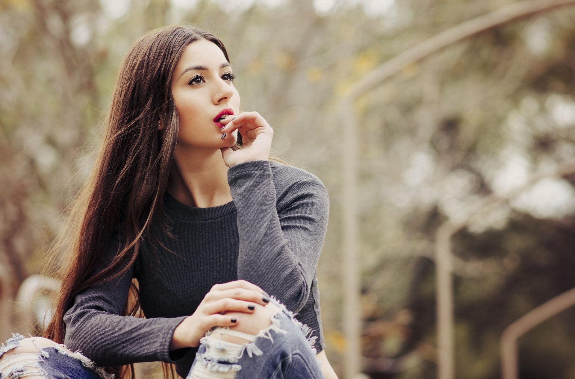 HD desktop wallpaper of a brunette woman with brown eyes and red lipstick, captured with a shallow depth of field against a soft, blurred natural background.