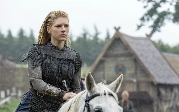 Blonde shieldmaiden in chainmail on a white horse in a Viking village, scene from Vikings (2013) TV show — 5K Ultra HD desktop wallpaper.