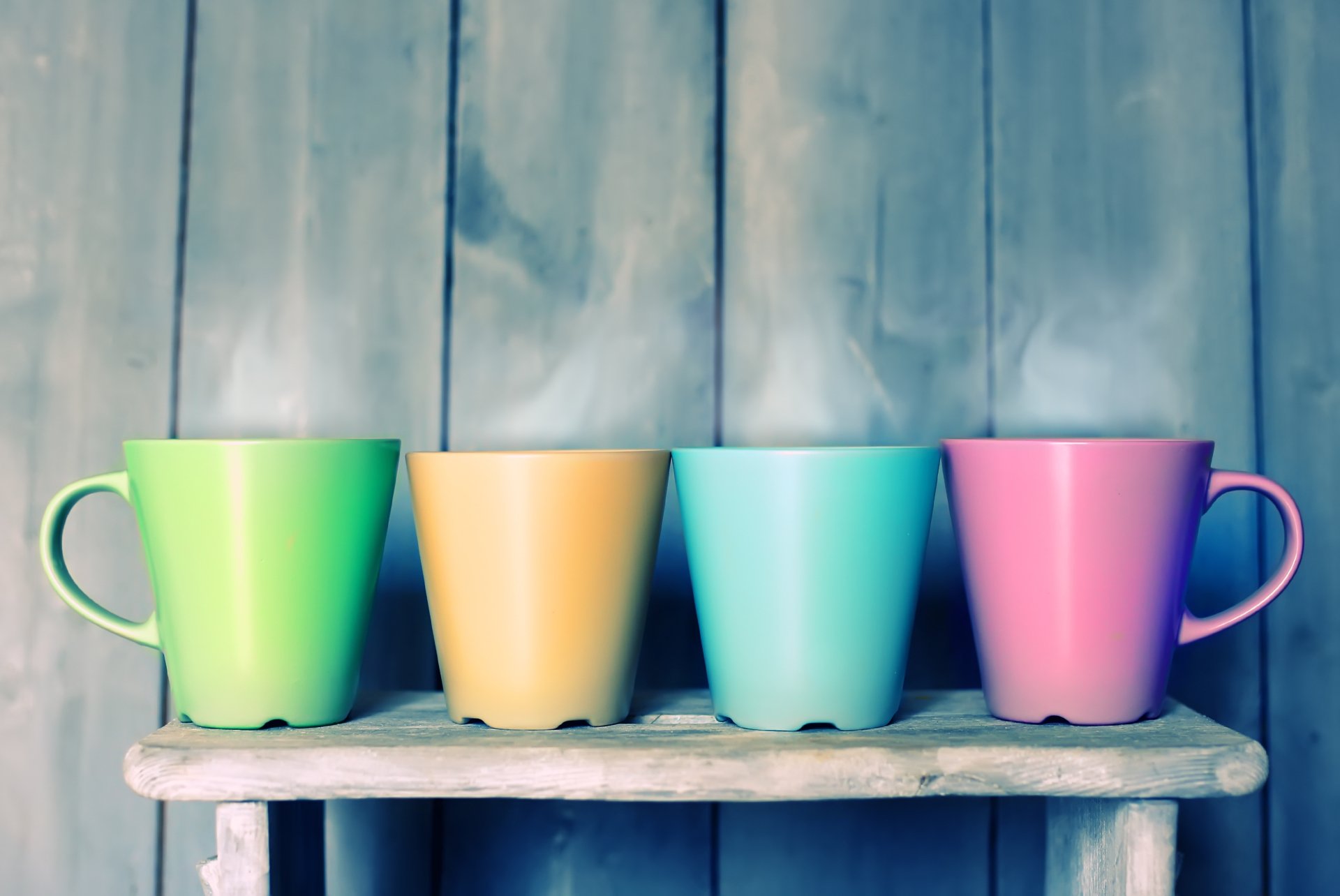 Four colorful man-made cups (green, yellow, teal, pink) on a rustic shelf against weathered wood — 5K Ultra HD PC desktop wallpaper and background.