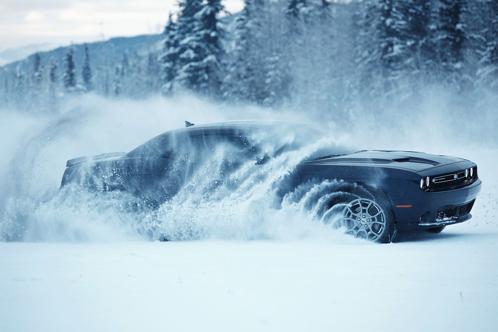 HD PC desktop wallpaper of a Mopar vehicle — Dodge Challenger GT AWD muscle car — plowing through deep snow with a snowy forest backdrop.