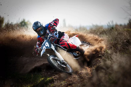 A motocross rider on a white motorcycle kicks up dirt while taking a sharp turn in an action-packed scene. The image is a HD desktop wallpaper suited for fans of motocross and extreme sports.