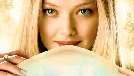HD PC desktop wallpaper for the movie Letters to Juliet: close-up of a blonde woman with green eyes peeking over a sheet, soft warm lighting, serene smile.