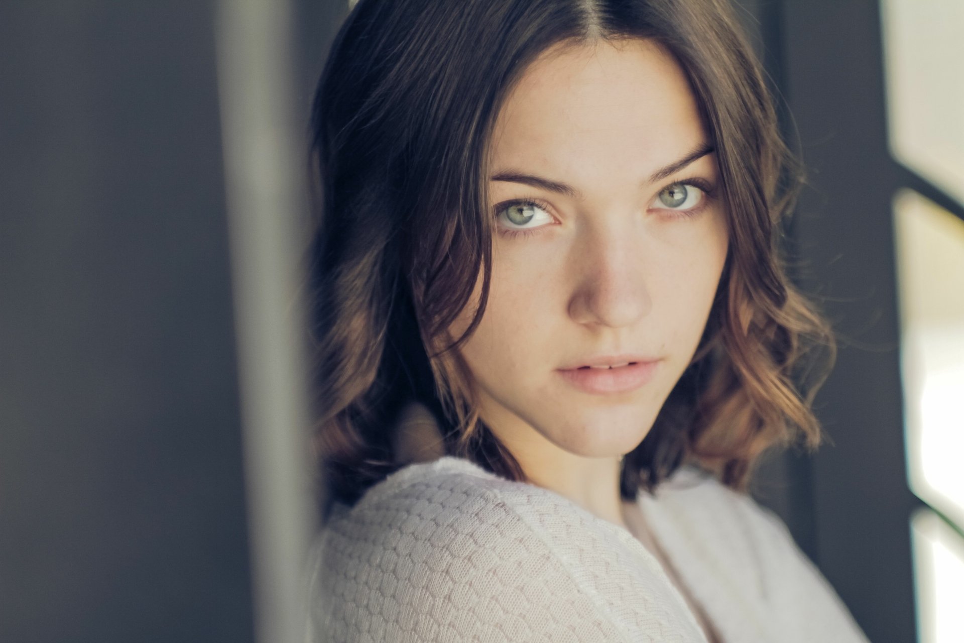 Close-up portrait of a brunette woman with green eyes and a soft expression, bathed in warm light — 5K Ultra HD PC desktop wallpaper.