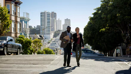 HD PC desktop wallpaper from TV show Murder in the First: two detectives stride up a sunlit San Francisco hill, skyline and row houses behind them.